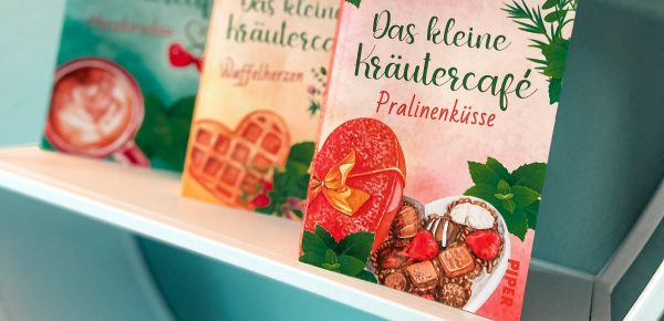 „Das kleine Kräutercafé — Pralinenküsse“ von Lilli Meinhardis, erschienen bei Between Pages by Piper ᵘⁿᵇᵉᶻᵃʰˡᵗᵉ ᵂᵉʳᵇᵘⁿᵍ, ᴿᵉᶻᵉⁿˢⁱᵒⁿˢᵉˣᵉᵐᵖˡᵃʳ